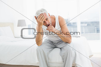 Thoughtful mature man yawning in bed