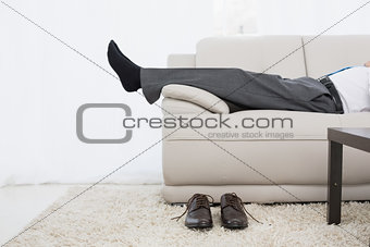 Low section of a businessman resting on sofa in living room