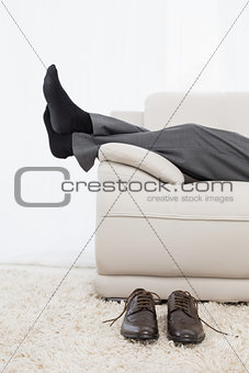Low section of businessman resting on sofa in the living room