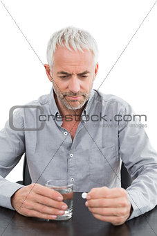 Serious mature man holding glass of water and pill at the table