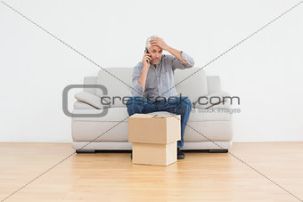 Annoyed man using cellpone on sofa with boxes in house