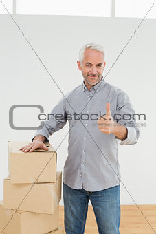 Smiling man with boxes gesturing thumbs up in a new house