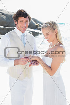 Man putting ring on smiling blonde brides finger