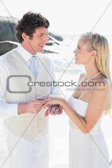 Handsome man putting ring on smiling blonde brides finger