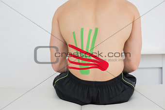 Shirtless man with red and green kinesio tapes on back