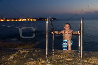 Night shot of boy getting out of the sea against the resort town