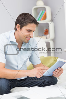 Smiling man with bills using digital tablet in the living room