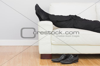 Low section of businessman resting on sofa in living room
