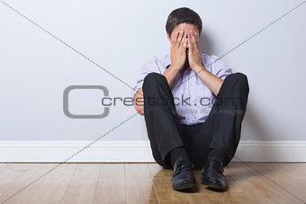 Businessman sitting on floor with hands covering face in empty room