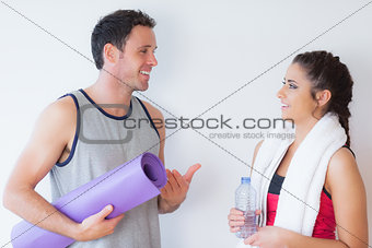 Fit young couple with towel and exercise mat chatting