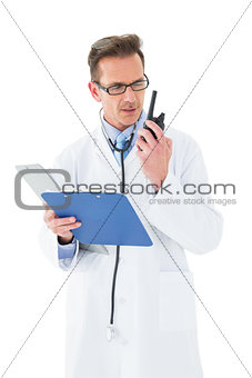 Serious doctor with clipboard talking on wireless radio