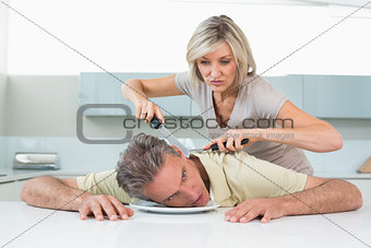 Angry woman holding knife to man's neck in kitchen