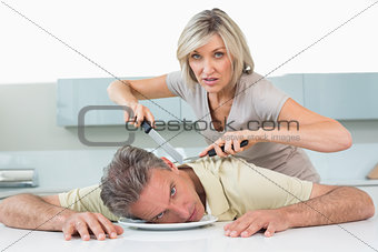 Angry woman holding knife to man's neck in kitchen