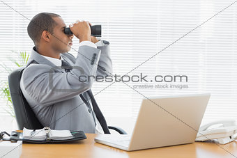 Businessman looking through binoculars at office desk
