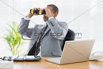 Businessman looking through binoculars at desk