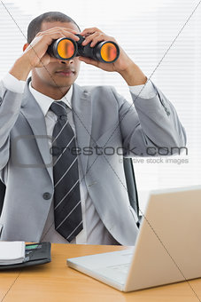 Businessman with binoculars in front of laptop at office