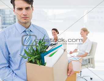 Businessman carrying his belongings with colleagues in background