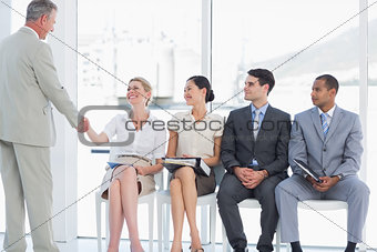 Businessman shaking hands with woman by people waiting for interview