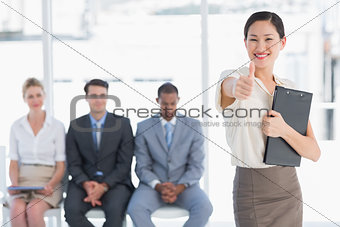 Woman gesturing thumbs up with people waiting for interview