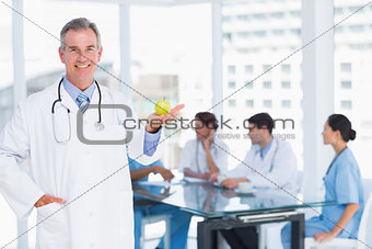 Doctor holding apple with group around table at hospital