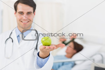 Smiling doctor holding apple with patient in hospital