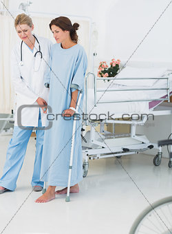 Full length of a doctor helping patient in crutches