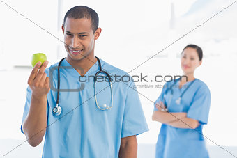 Male surgeon holding an apple with colleague behind