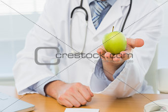 Mid section of a male doctor holding an apple