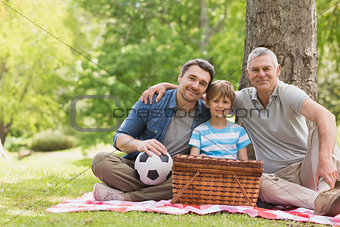 Grandfather, father and son with picnic basket at park