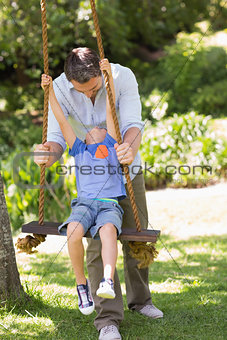 Happy father pushing boy on swing