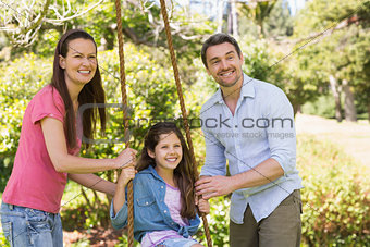 Happy couple pushing daughter on swing