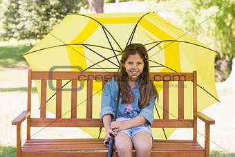 Girl sitting on park bench with an umbrella