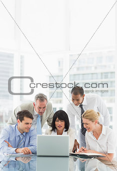 Happy business people gathered around laptop discussing