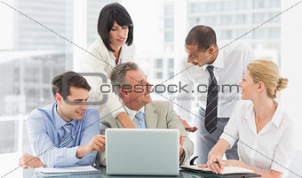 Happy business team gathered around laptop talking