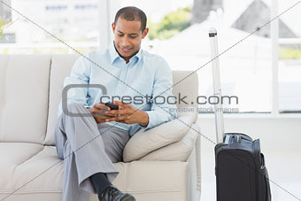 Man sitting on sofa sending a text waiting to depart on business trip