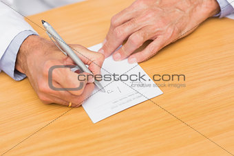 Doctor sitting at his desk writing on prescription pad