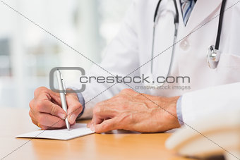 Doctor sitting at his desk writing a prescription