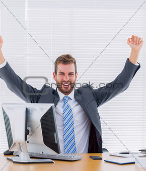 Cheerful businessman clenching fist at office desk