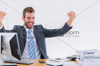 Cheerful businessman clenching fist computer at office desk