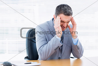 Businessman with severe headache at office desk