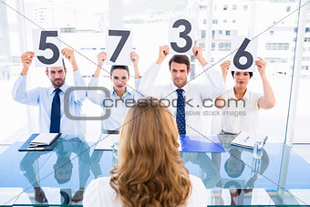 Group of panel judges holding score signs in front of a woman