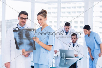 Doctors examining xray with colleagues using laptop behind