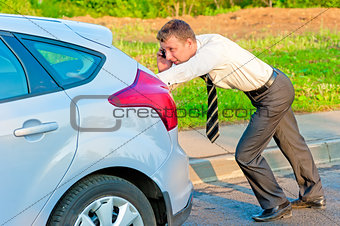 Businessman pushing a car and talking on the phone 