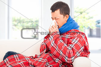 ill man blowing nose with tissue on sofa at home