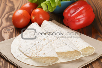 wheat tortillas with vegetables on old wooden table