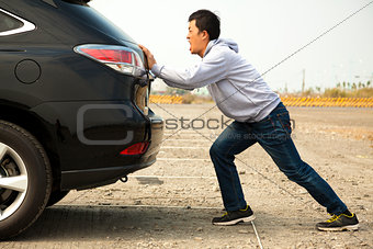 Man pushing a broken car down the rock road 