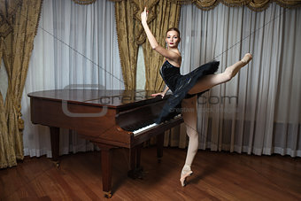 Ballerina in black tutu standing on pointes at grand piano