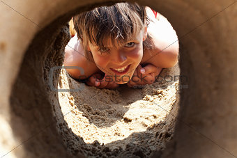 Happy boy on the beach looking through sand castle tunnel