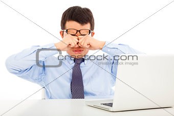 tired young businessman rubbing his eyes with laptop