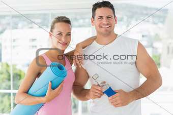 Fit couple holding water bottle and exercise mat in exercise room